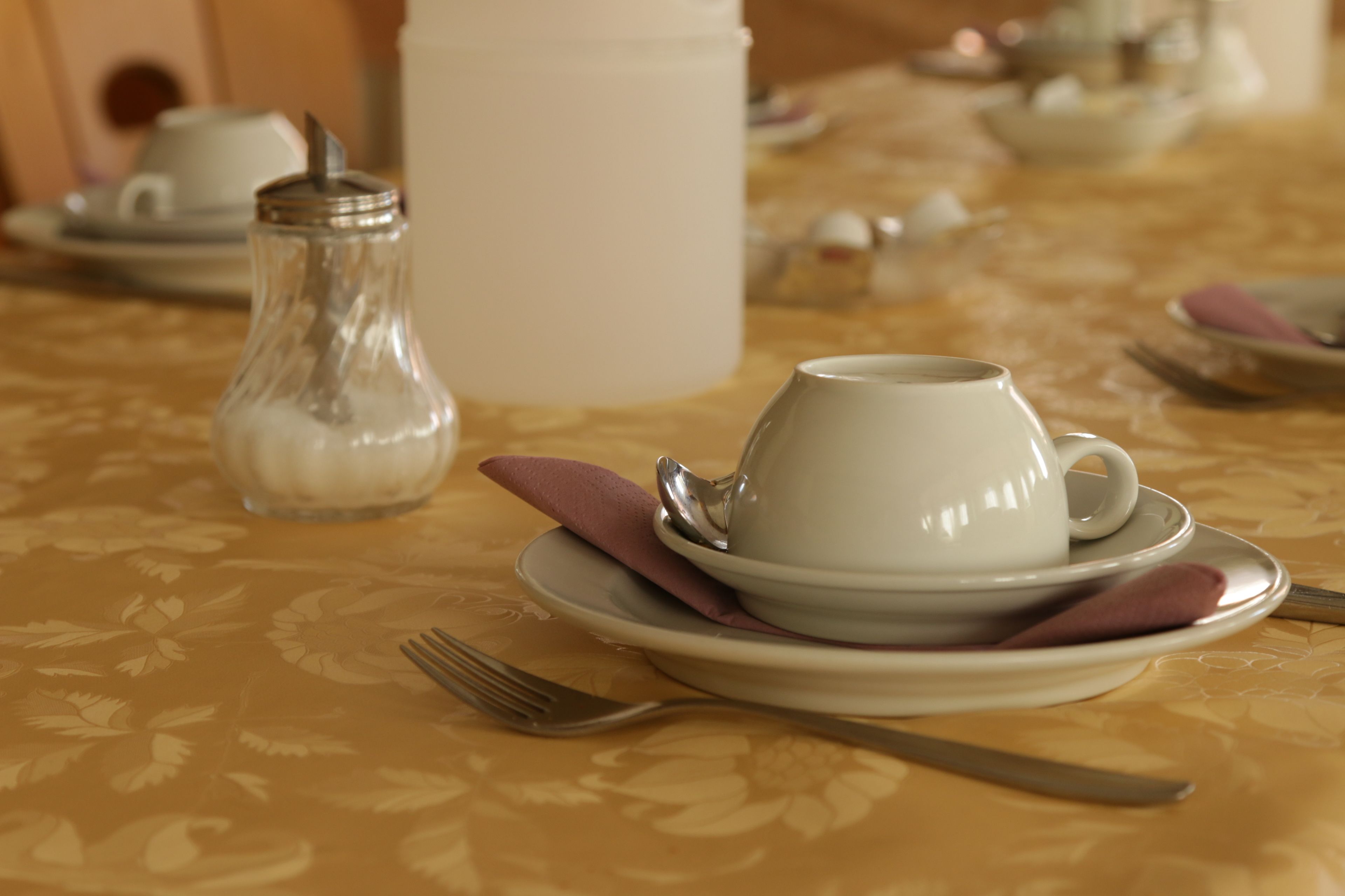 Una tavola apparecchiata con una tazza bianca, un piattino e una brocca di vetro con coperchio.