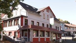 A two-story building with a red and white facade, a covered outdoor seating area, and a sign indicating a price of 5.00€. - Hotel-Ristorante Ätna (Ulrichstein)
