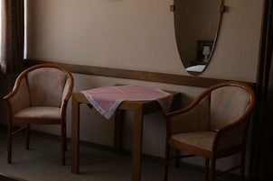 Um quarto com duas cadeiras de madeira, uma mesa pequena com toalha de mesa rosa e um espelho na parede.