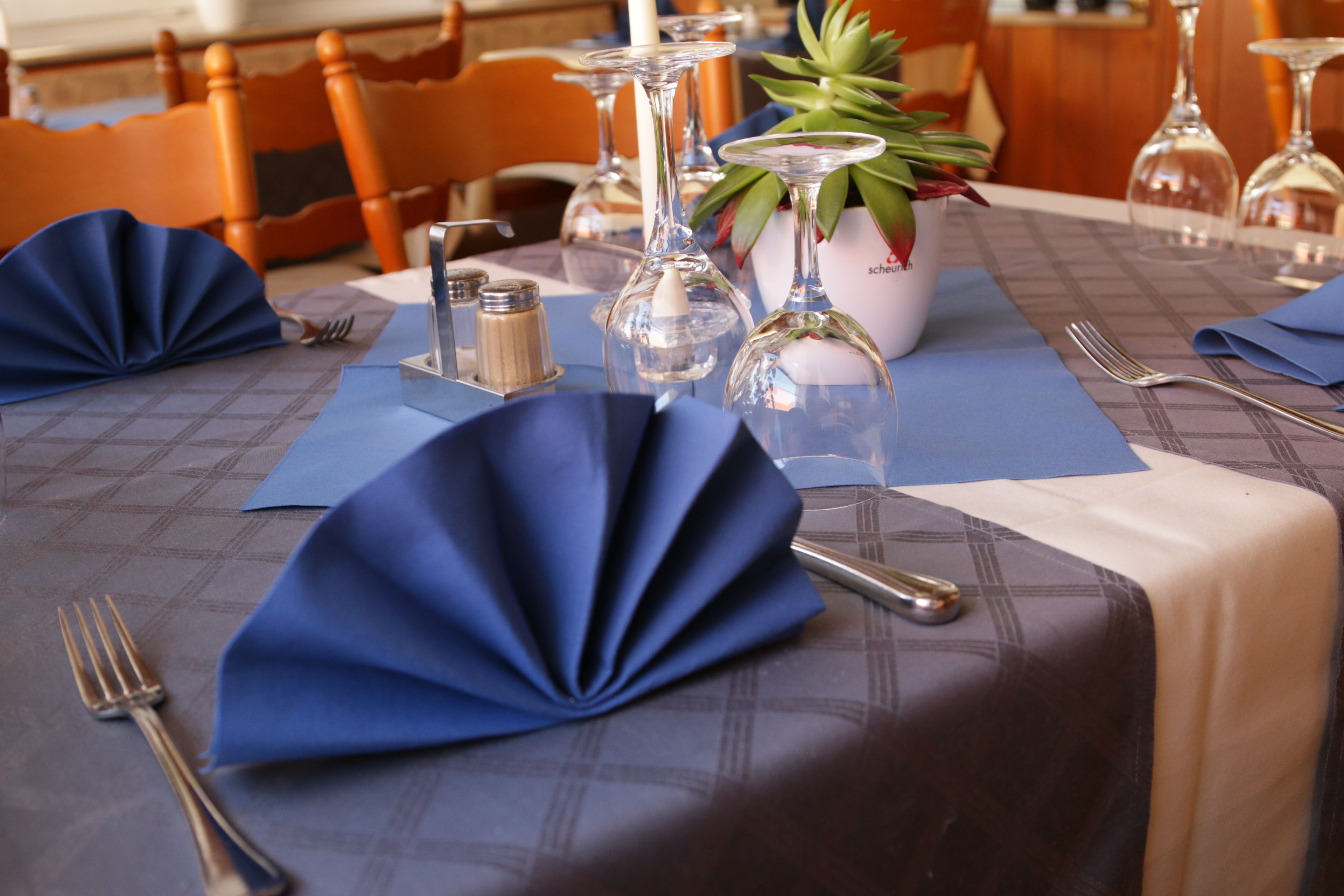 Una mesa dispuesta para comer, con servilletas azules, cubiertos y copas de vino.