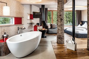 Un baño moderno con una bañera grande, piso de madera y vistas al bosque.