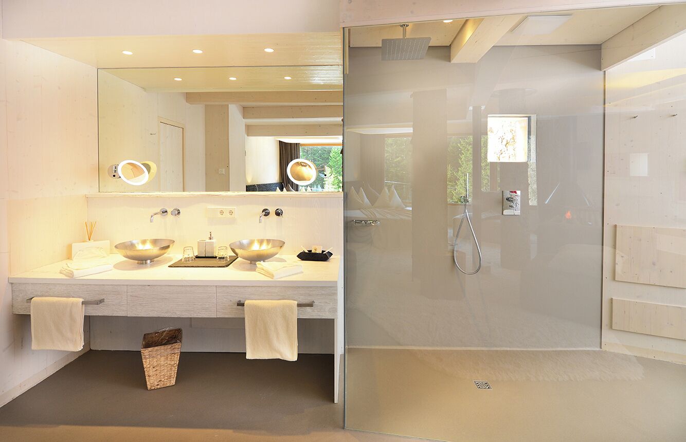 Une salle de bain moderne avec un grand miroir, deux lavabos, une douche et un espace douche fermé par des parois de verre.