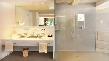 Une salle de bain moderne avec un grand miroir, deux lavabos, une douche et un espace douche fermé par des parois de verre.