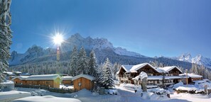 Un refugio invernal cubierto de nieve con cabañas de madera, un edificio central grande y una vista despejada de picos nevados al fondo.