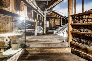 A wooden cabin with a snow-covered exterior, a wooden staircase leading to a door, and a stack of firewood on the right. - Caravan Park Sexten (Sesto)