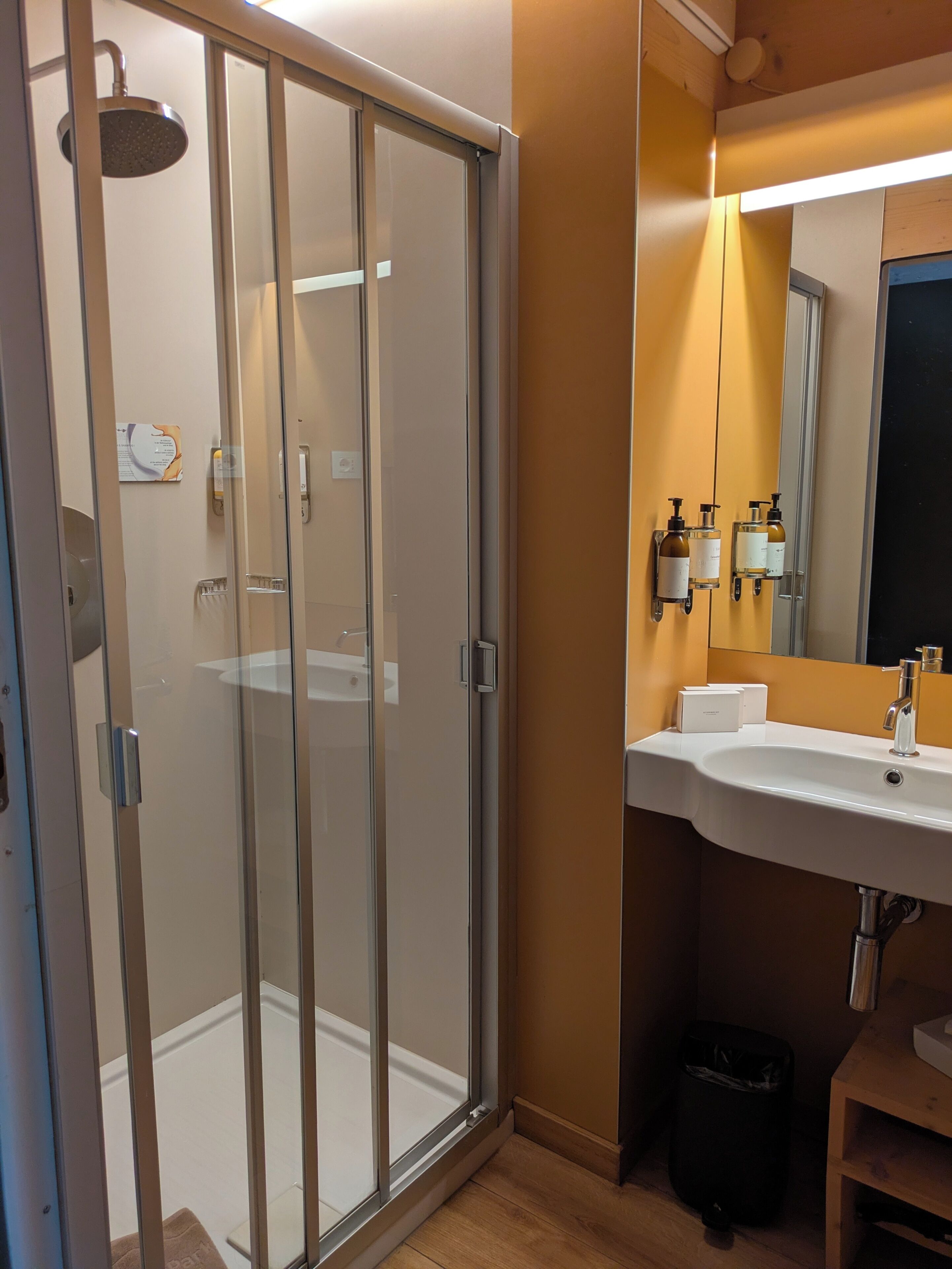 A modern bathroom with a glass-enclosed shower, a sink with soap dispensers, and a mirror above the sink.