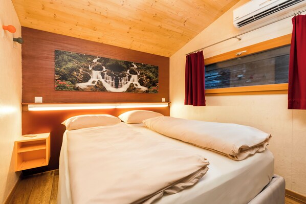 Une chambre à coucher avec un lit, une table de chevet, un climatiseur fixé au mur, une fenêtre avec des rideaux et un tableau au-dessus du lit.