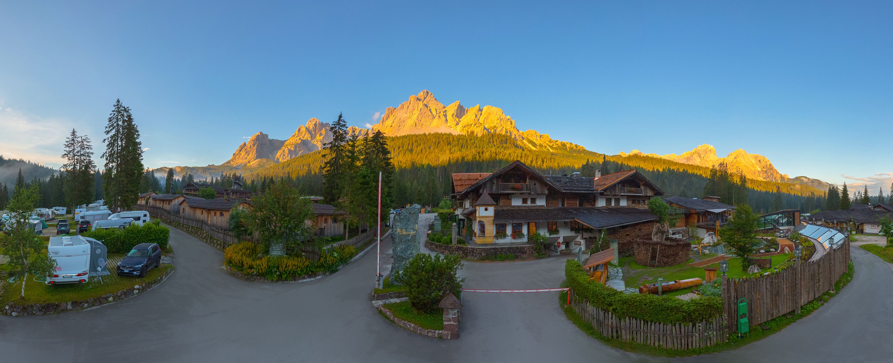 Un village de montagne avec des maisons traditionnelles en bois, un parking pour camping-cars et une montagne imposante en arrière-plan.