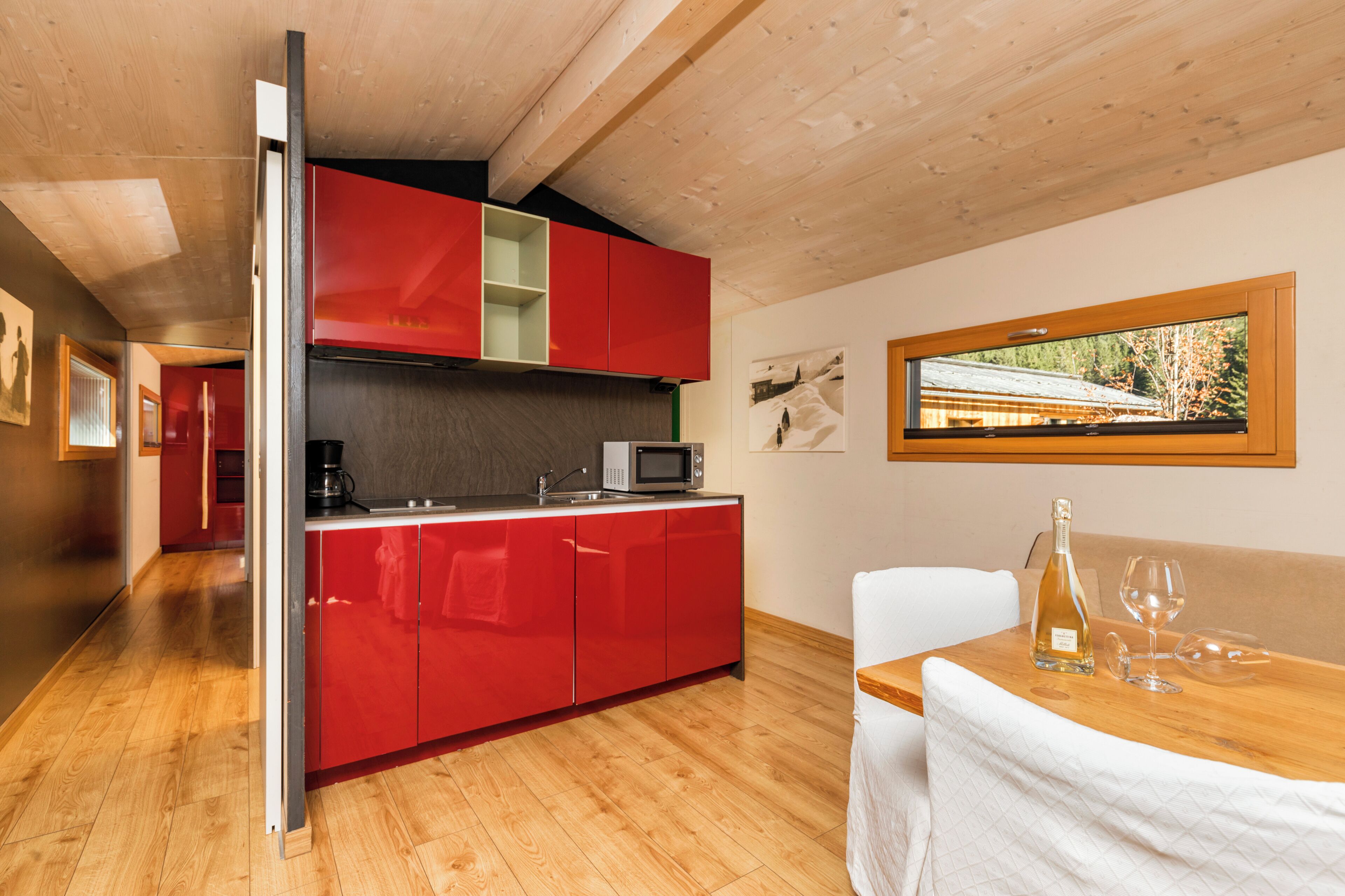 Una cocina moderna con armarios rojos, un microondas y una zona de comedor con una mesa preparada para dos personas.