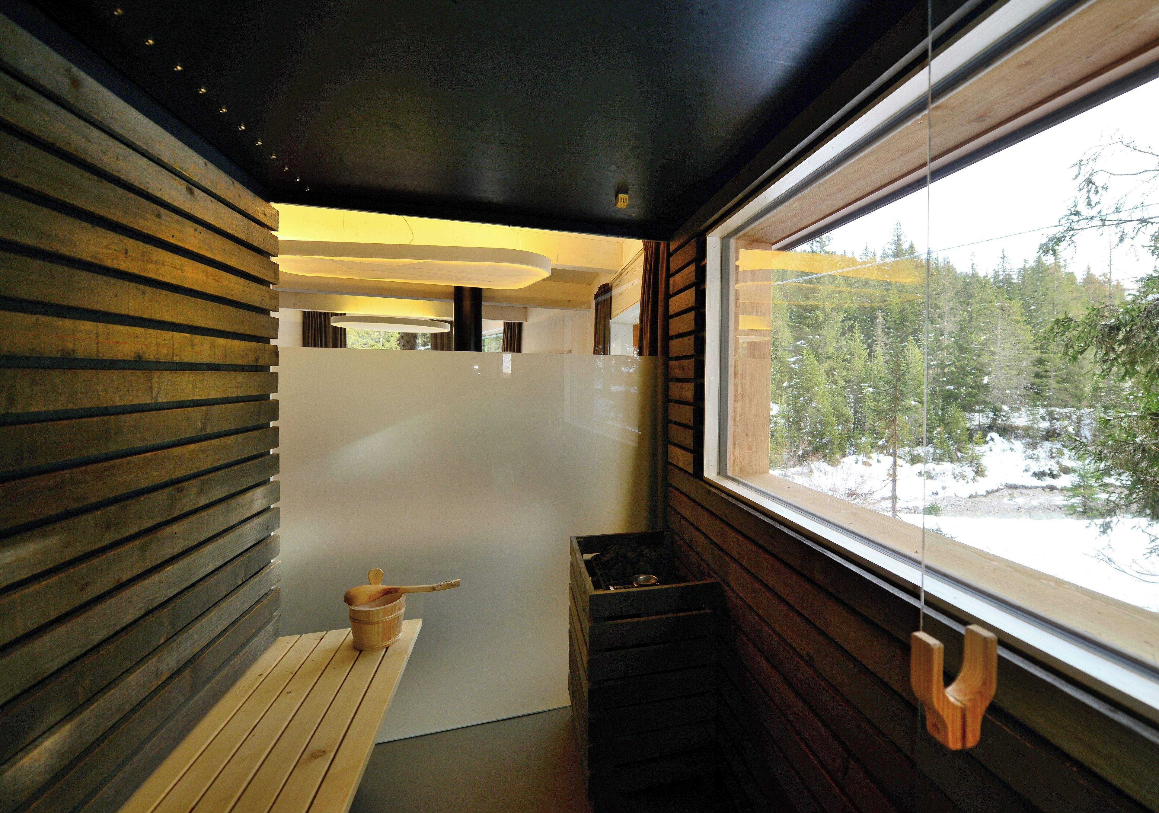A modern interior with wooden slats on the walls, a bench, and a window with a view of a snowy forest.