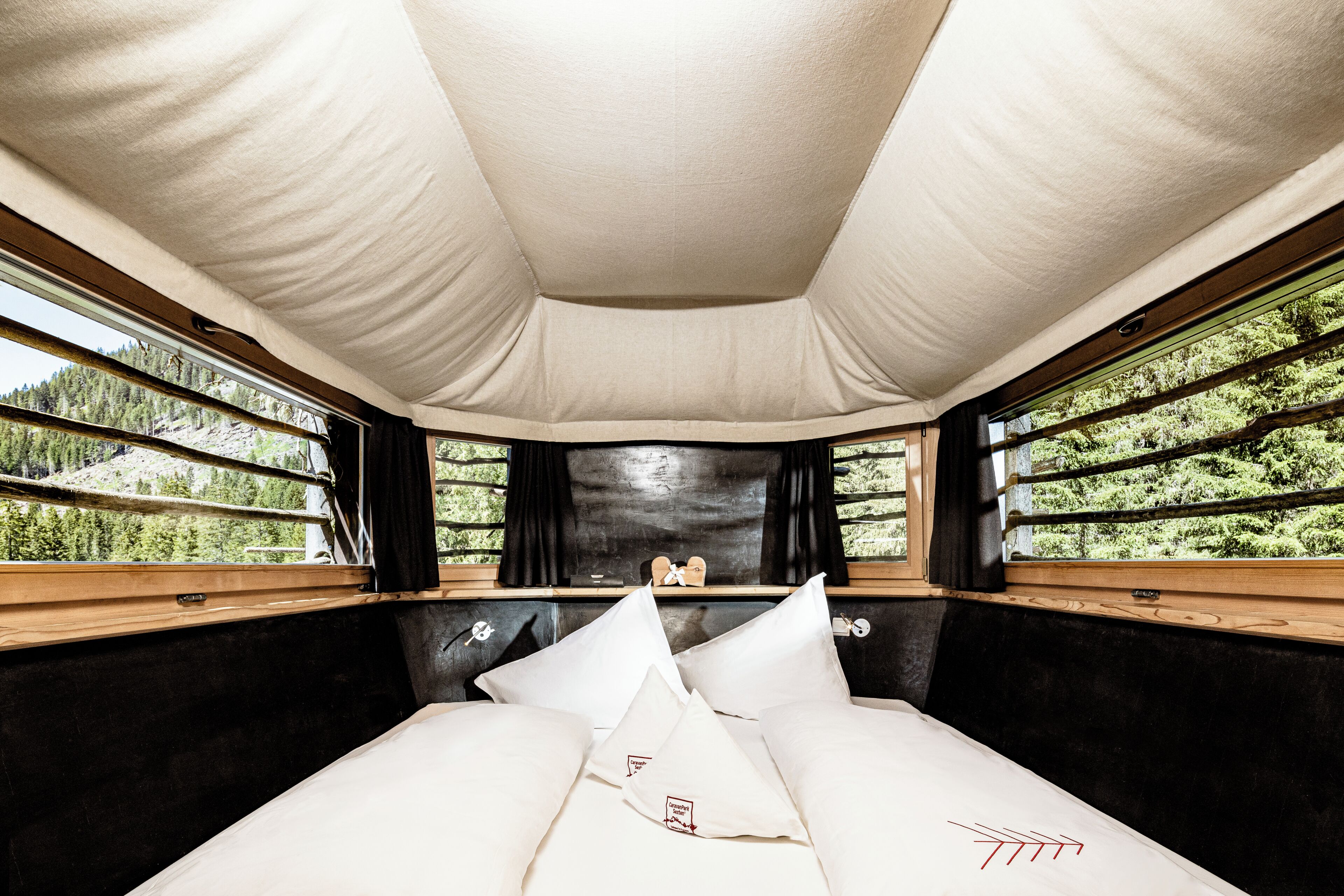 A bed with white linens and a headboard, a window with a view of trees, and a ceiling with a light fixture.