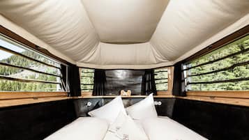A bed with white linens and a headboard, a window with a view of trees, and a ceiling with a light fixture.