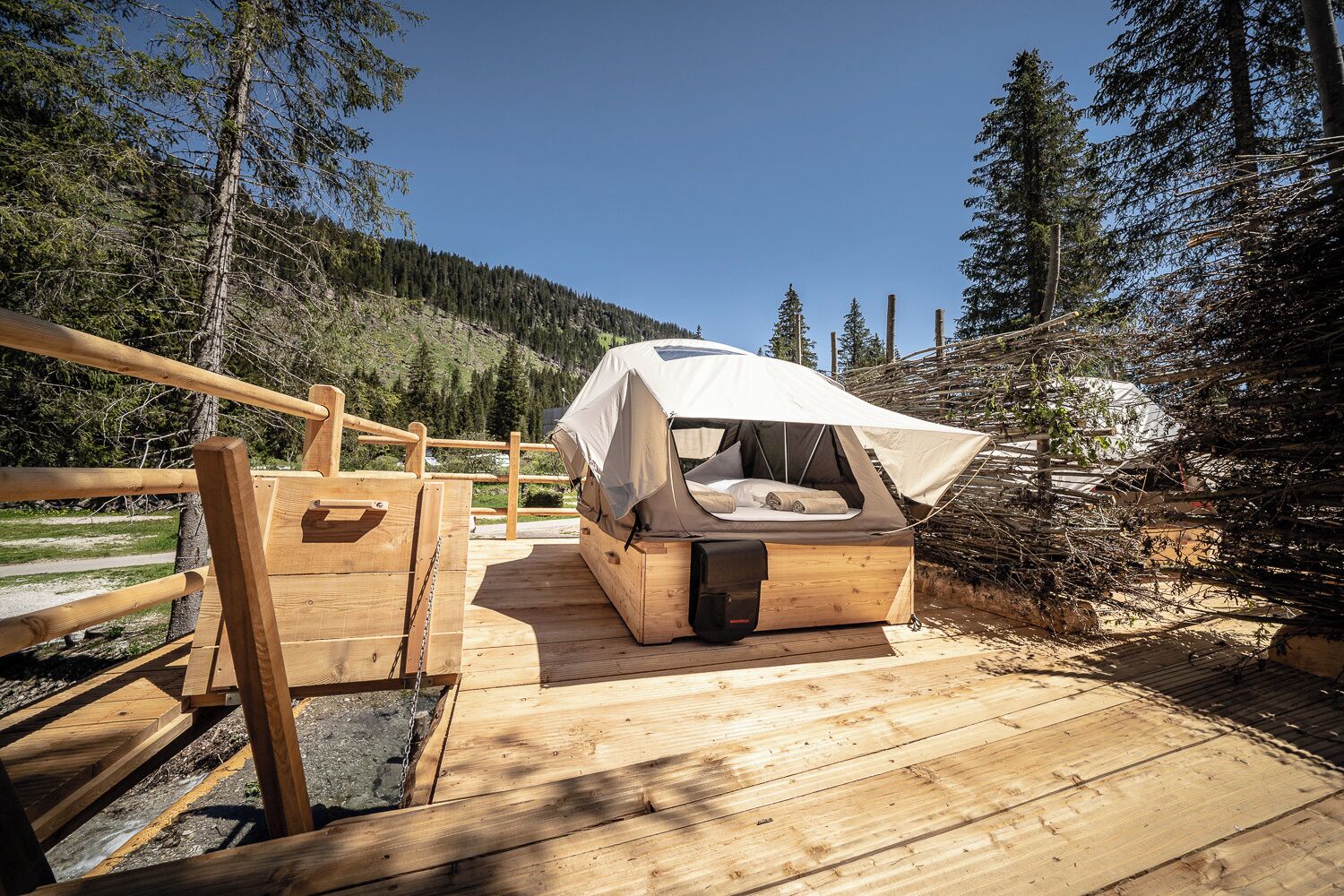 A wooden deck leading to a tented accommodation with a view of a forested hillside.