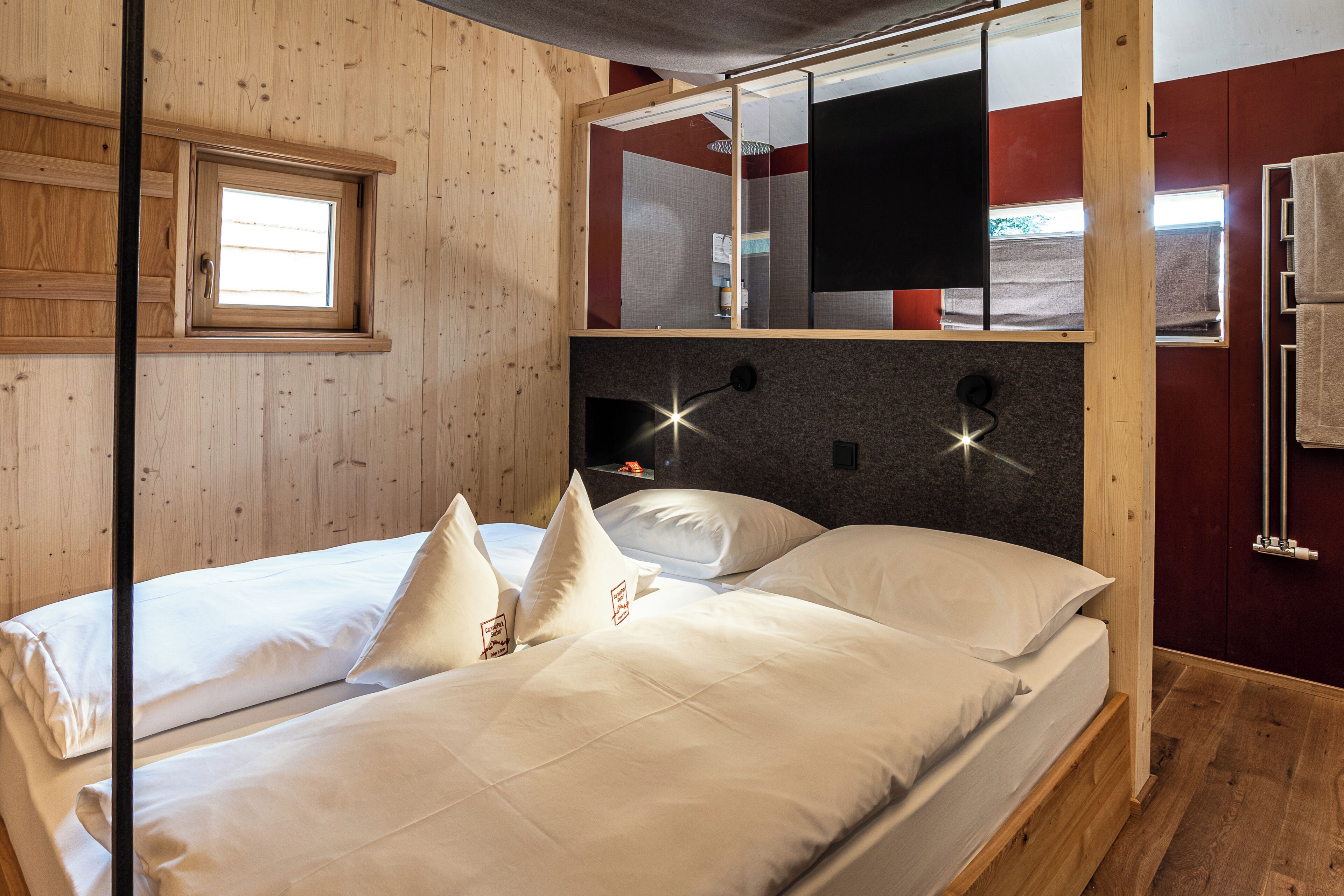 Een kamer met houten vloeren, een bed, een raam en een spiegel.