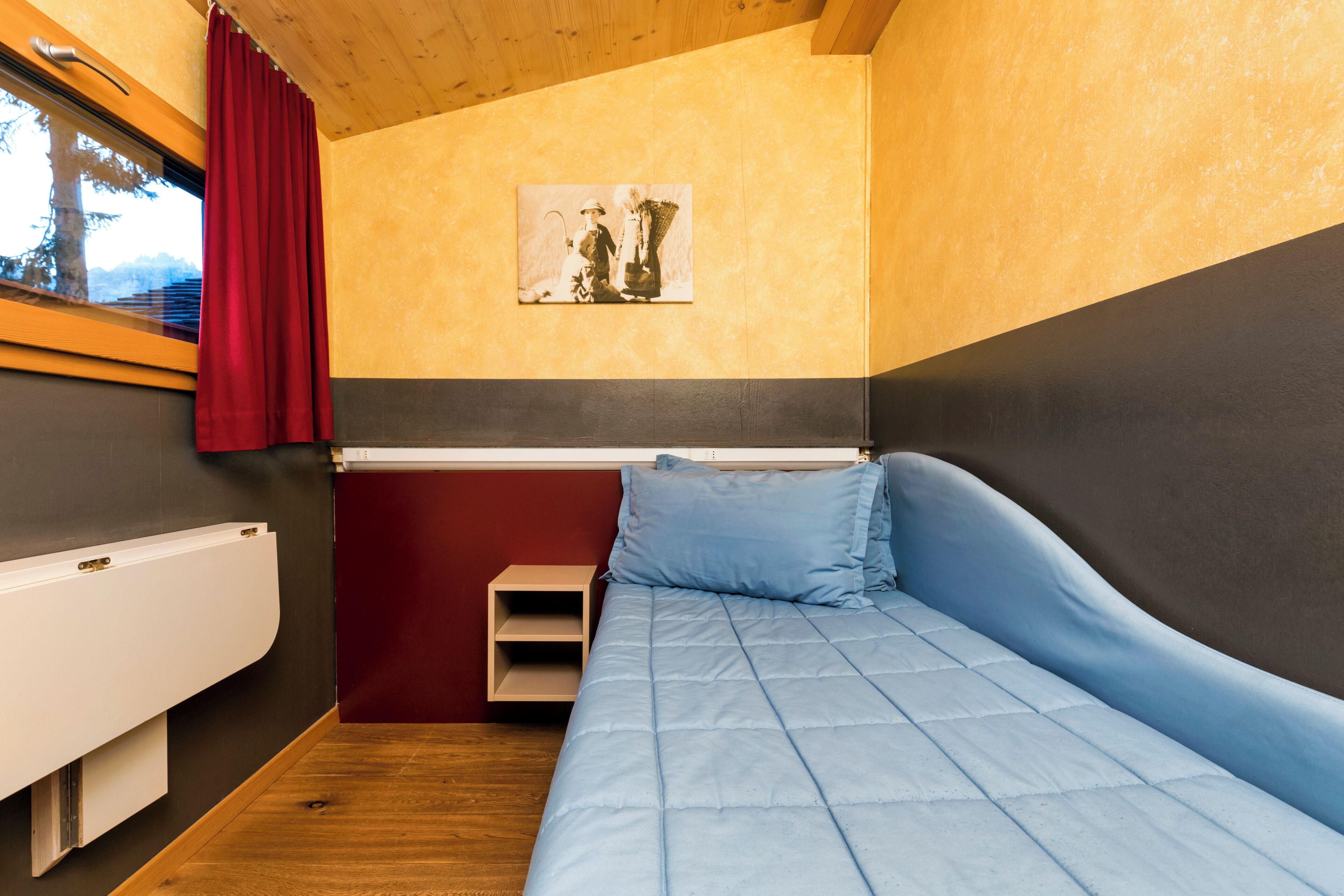 Ein kleines Schlafzimmer mit einem Einzelbett, einem Nachttisch, einem Heizkörper und einem Fenster mit Vorhängen.