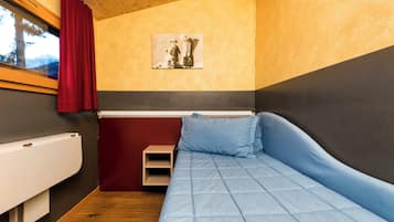 Ein kleines Schlafzimmer mit einem Einzelbett, einem Nachttisch, einem Heizkörper und einem Fenster mit Vorhängen.