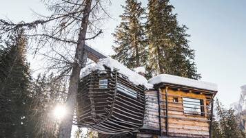 A wooden cabin elevated on stilts in a snowy forest.