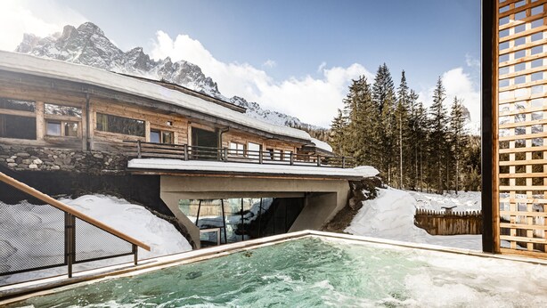 Uma área de spa com hidromassagem, deck de madeira e vista para montanhas cobertas de neve.