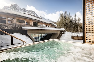 Zona de spa con hidromasaje, terraza de madera y vistas a montañas nevadas.