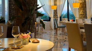 A dining area with a table set for two, a potted plant, and a view of the outdoors.