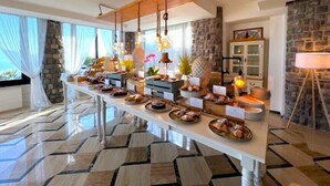 A buffet setup with various food items and a long table in a well-lit room with stone walls and large windows. - Romantic Relais Sorrento (Sorrento)