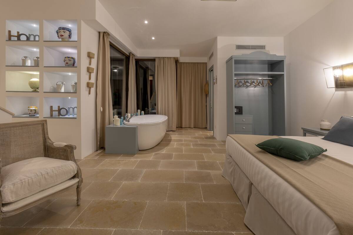 Una habitación de hotel moderna con una cama grande, una silla, una tocador con espejo, una bañera y un armario.