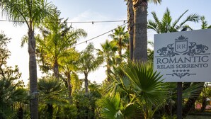 A sign for 'Romantic Relais Sorrento' amidst a lush garden with palm trees and a pathway. - Romantic Relais Sorrento (Sorrento)