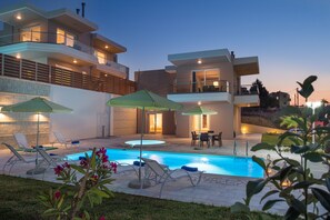 Una casa moderna de dos pisos con piscina, mobiliario exterior y un patio bien iluminado.