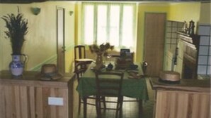 Un comedor con mobiliario de madera, mantel verde y una ventana con persianas.