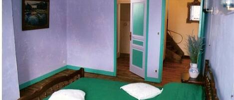 A room with two beds, a painting on the wall, and a staircase leading to another room.
