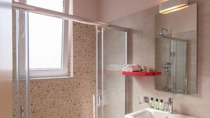 A bathroom with a glass shower enclosure, a sink with toiletries, and a mirror above the sink.