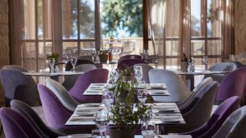 A dining area with tables set for four, each with a potted plant, wine glasses, and cutlery.