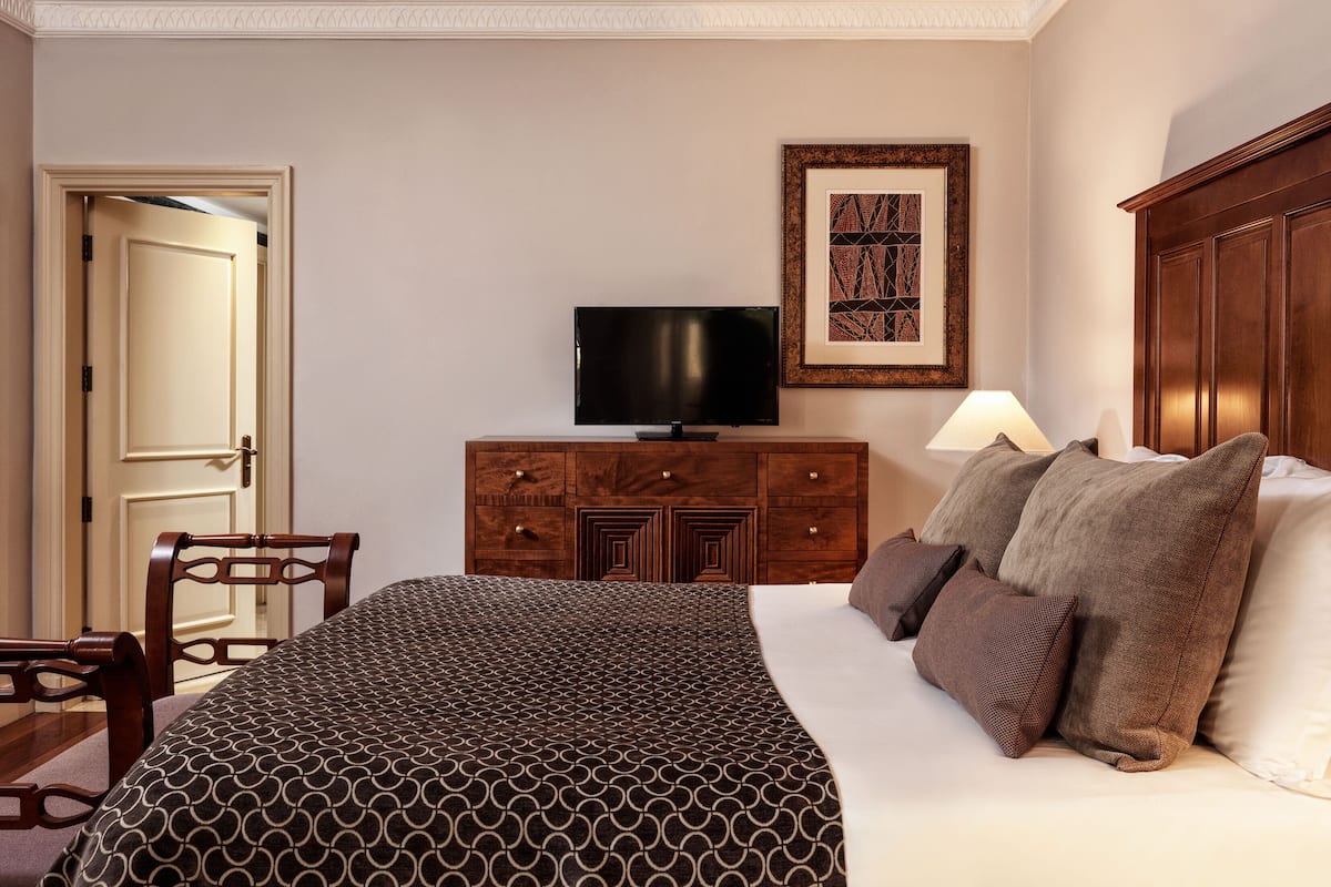 A hotel room with a bed, a television on a wooden dresser, a door, and a framed picture on the wall.