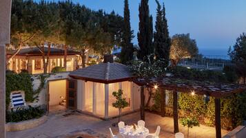 Un área de comedor al aire libre con mesas y sillas redondas, una piscina pequeña y una pérgola.