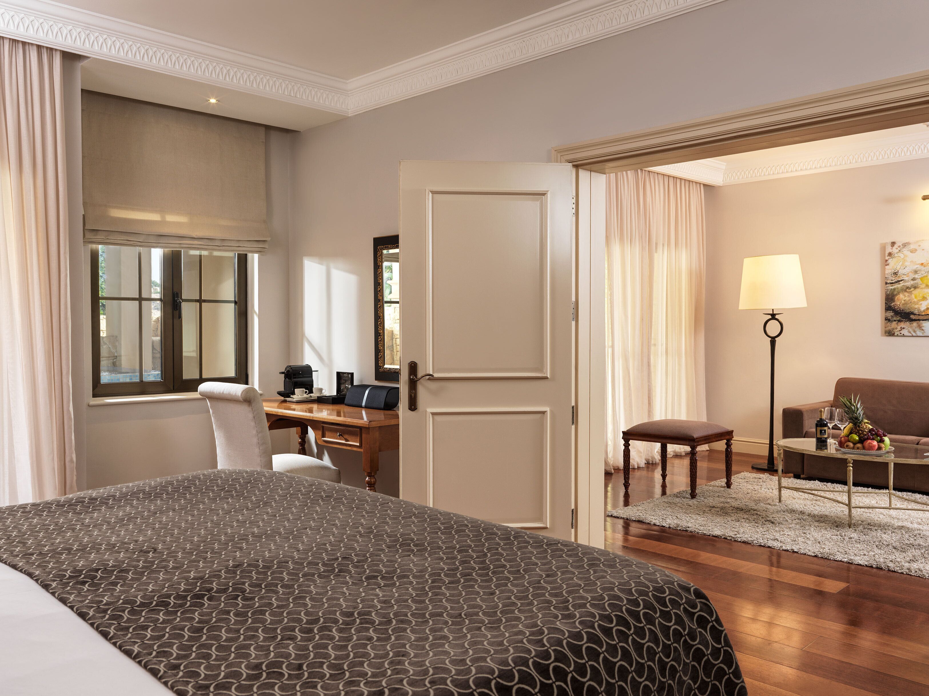 A hotel room with a large bed, a desk with a chair, a sofa, a coffee table, and a lamp.