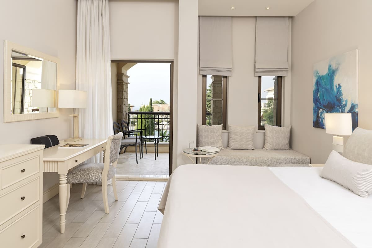 A hotel room with a bed, a desk, a chair, a balcony, and a painting.