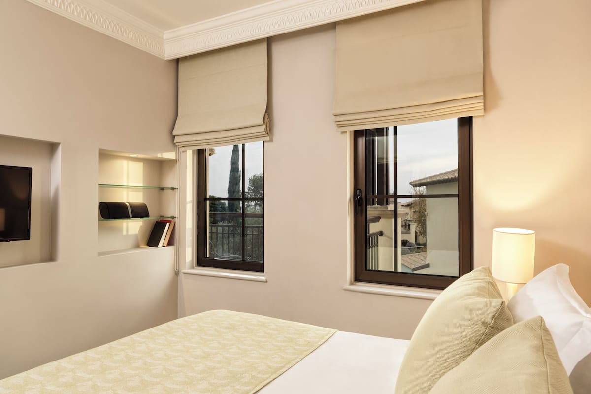 A hotel room with a bed, a window with a view, a bedside table with a lamp, and a wall-mounted TV.