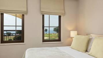 A bedroom with a bed, two windows with views of a golf course and the ocean, and a nightstand with a lamp.