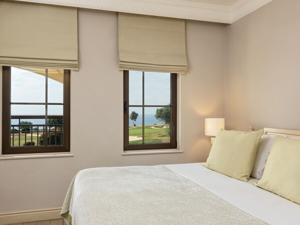 Un dormitorio con cama, dos ventanas que dan a un campo de golf y al océano, y una mesita de noche con lámpara.