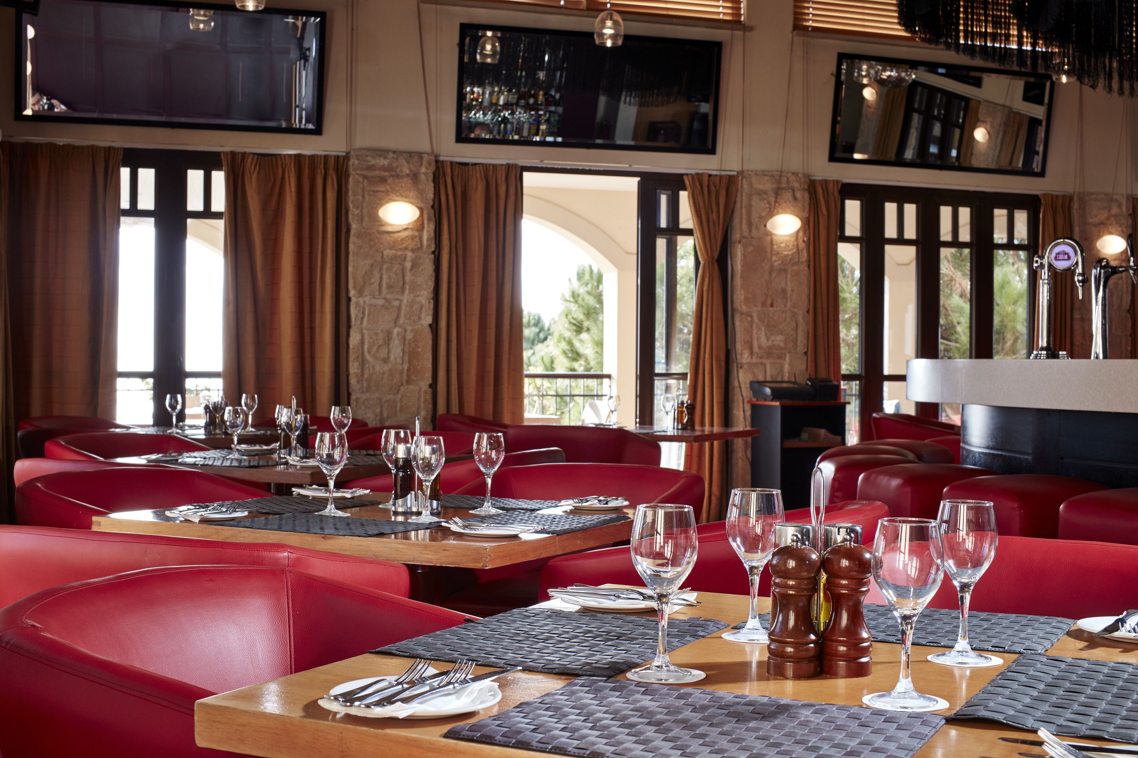 A restaurant with red leather booths and tables, each set with wine glasses and cutlery.