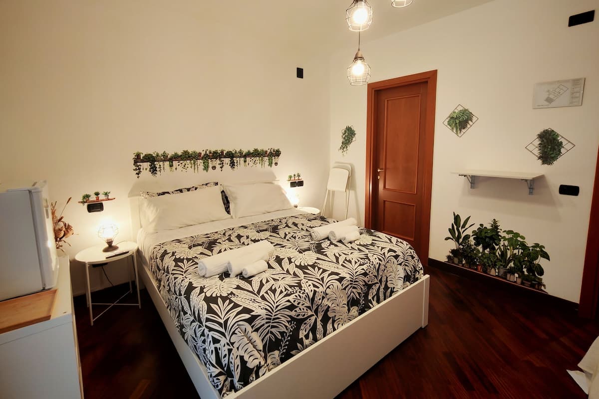 A bedroom with a bed, bedside tables, a wardrobe, a door, and wall-mounted shelves with plants.