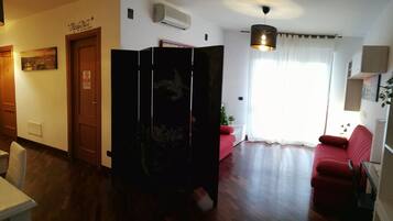 Sala de estar con un sofá rojo, una mesa de comedor con sillas, una zona de cocina y un ventanal con cortinas.