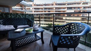 En balkong med en soffa, ett bord och en stol, med utsikt över en flervåningsbostadsbyggnad.
