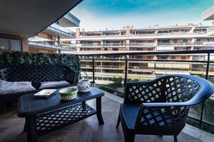 Un balcón con sofá, una mesa y una silla, con vista a un edificio residencial de varios pisos.