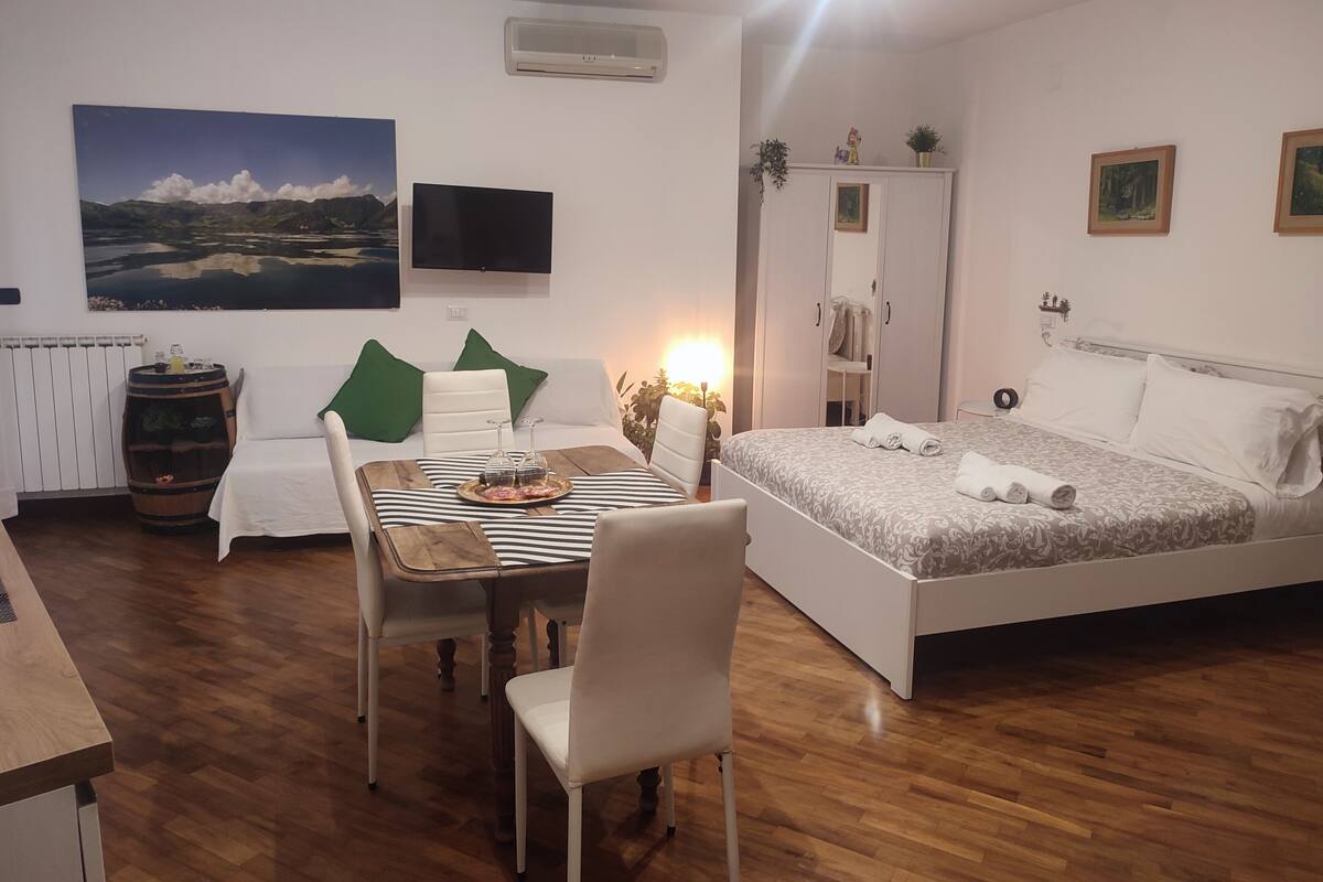 A bedroom with a bed, a bedside table, a chair, a sofa, a TV, and a painting on the wall.