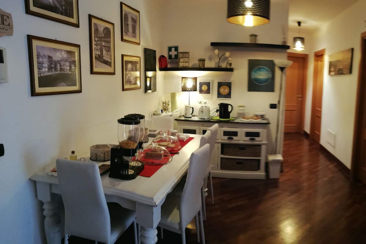 A narrow hallway with a kitchen area on the left, featuring a dining table with chairs, a refrigerator, and various kitchen appliances.