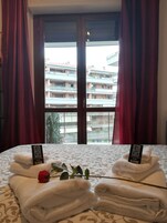 Habitación de hotel con una cama, dos toallas, una rosa y un cartel sobre la cama.