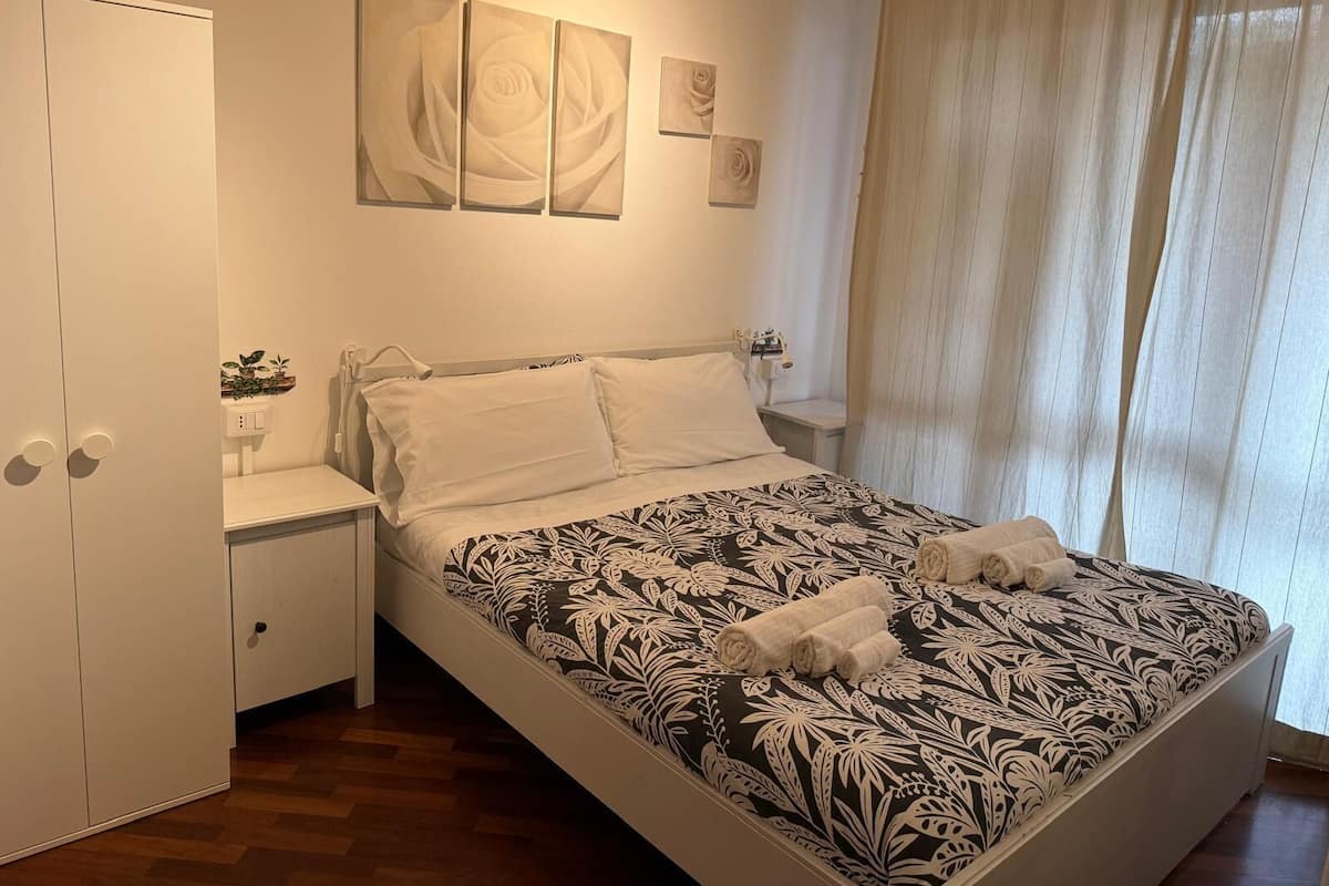 A bedroom with a bed, a nightstand, a wardrobe, and a window with curtains.