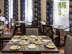 A dining area with tables set for service, chairs, and curtains with a pattern.