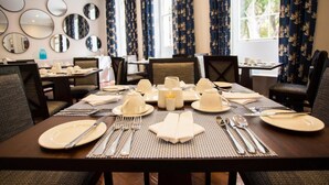 A dining area with a table set for four, surrounded by chairs, with a window and curtains in the background. - Mantis St Helena (Jamestown)